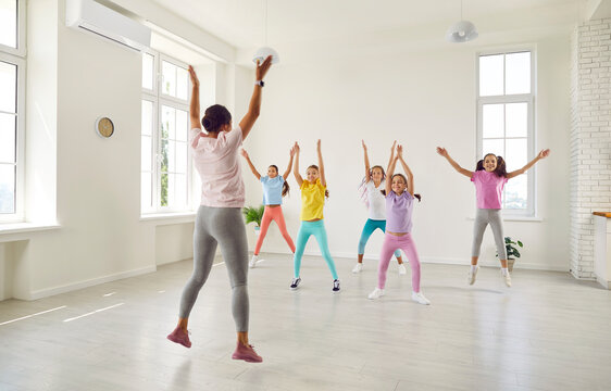 Smiling happy girls training modern dance moves together in studio with female choreographer. Group of kids doing dance workout in choreography class. Children sport and active lifestyle concept.