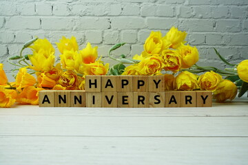 Happy Anniversary alphabet letters with flowers bouquet on wooden background