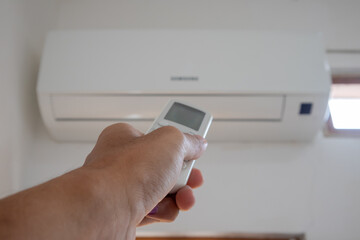 Fototapeta premium Hand holding AC remote control directed on the air conditioner inside the room