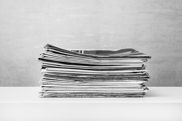 a stack of newspapers on a white table on a grey background, black and white photo