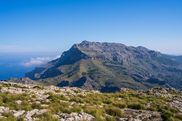 Amazing landscapes of Mallorca. The mountains are covered with greenery, the sea is blue and transparent. Sunny day, clouds over a rocky ridge. Mallorca, Spain, Balearic Islands