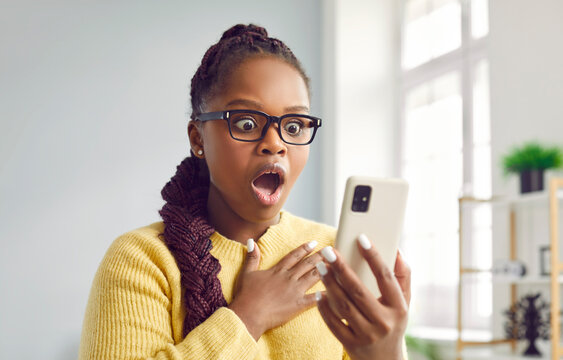 WOW. Beautiful woman looks at mobile phone with surprised open mouthed expression as she wins prize, earns money, sees unbelievable post on social media, watches shocking video, or finds special offer