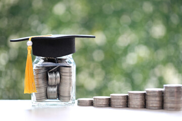 Graduation hat on coins money in the glass bottle on natural green background, Saving money for...