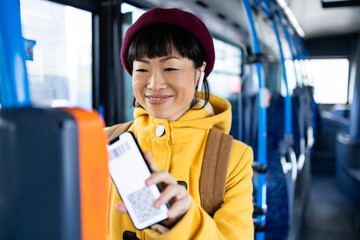 Female passenger using smart phone to validate ticket inside public bus transportation. - obrazy, fototapety, plakaty