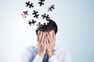Worried puzzle headed thoughtful businessman covering face with hands on light background with mock up place. Solution, decision and brainstorm concept.
