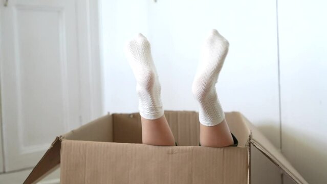 Zoom on child feet in white socks moving with a music into a big box, preparing to move house, white background. . High quality FullHD footage