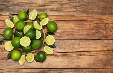 Fresh limes and green leaves on wooden table, flat lay. Space for text
