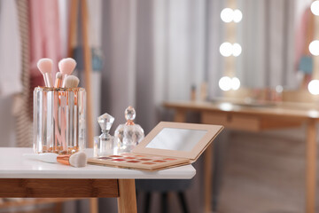 Set of brushes, eyeshadow palette and perfumes on white table in makeup room, space for text