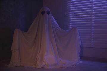 Creepy ghost. Woman covered with sheet near window in color lights