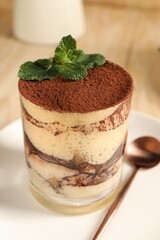 Tasty tiramisu and mint in glass on table, closeup