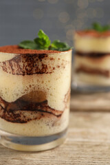 Tasty tiramisu and mint in glass on wooden table, closeup