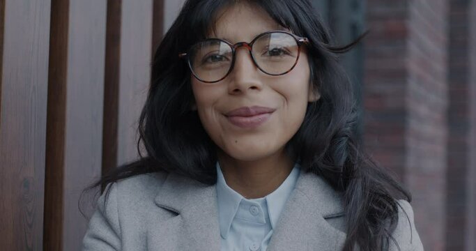Close-up portrait of happy Middle Eastern business lady putting on eyeglasses and smiling outdoors in city. Trendy eyewear and businessperson concept.