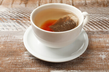 Tea bag in cup with hot drink on wooden rustic table, closeup