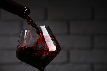 Pouring tasty red wine from bottle into glass against brick wall, closeup. Space for text