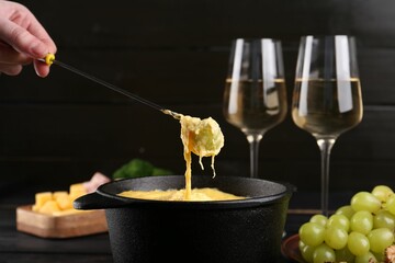 Dipping grape into fondue pot with melted cheese on table, closeup