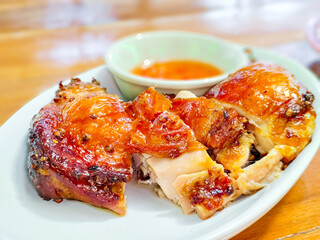 Thai style grilled chicken with herb on white dish on wooden table. Delicious food concept.