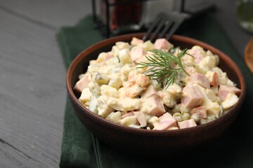 Tasty Olivier salad with boiled sausage in bowl on grey table, closeup. Space for text