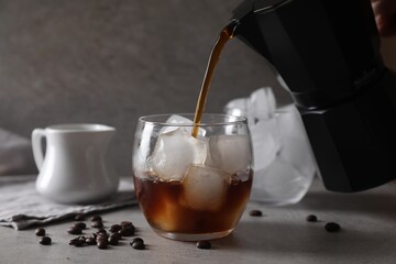 Woman pouring coffee into glass with ice cubes at gray table, closeup
