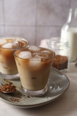 Refreshing iced coffee with milk in glasses, ingredients and spoon on light table, closeup