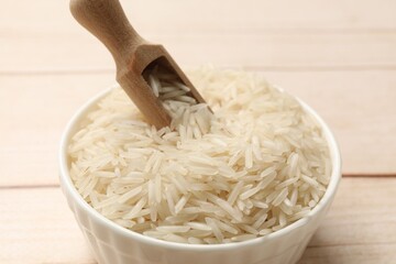 Raw basmati rice and scoop in bowl on white wooden table, closeup