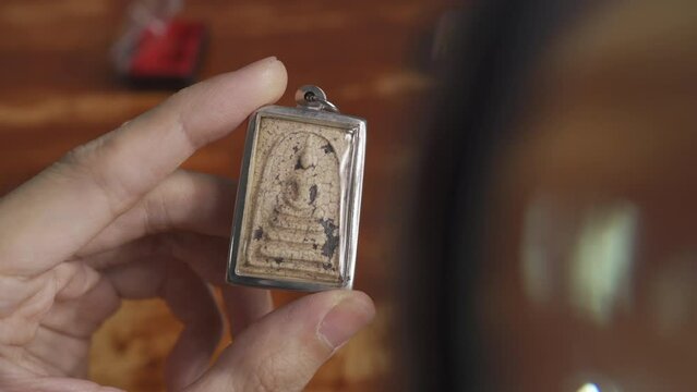 Using a magnifying glass to see the detail on an old Thai Buddha amulet