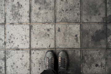 Man standing on the square shaped concrete pavement slabs, top view of dirty boots on dirty sidewalk