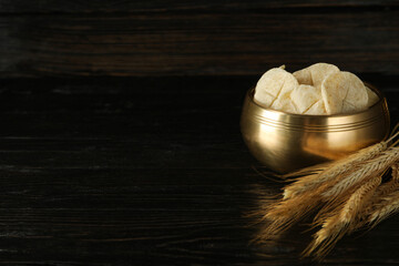 Bread in golden bowl and spikelets on dark wooden background, space for text