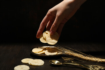 Bread in hand, spikelet and cutlery on dark background, close up