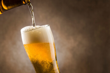 Pouring lager beer into glass with foam on dark background.