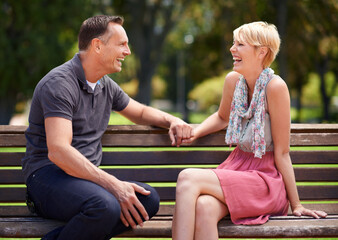 Love, laughing and happy couple on a park bench with funny conversation, gossip or bonding outdoors...