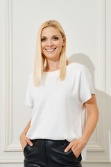 Fototapeta premium Positive woman in a white top and black leather pants, posing in front of a white wall