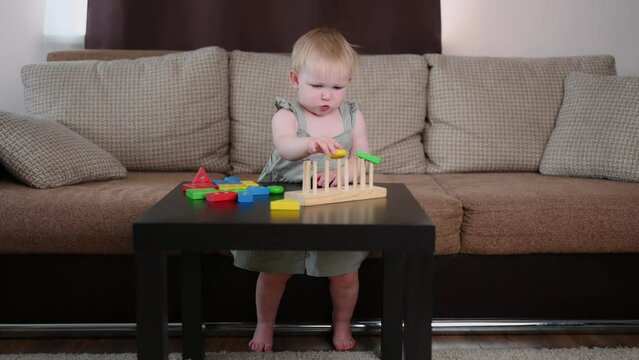 Toddler plays with a wooden educational toy while sitting on the sofa at home. Montessori games for child development. Concept of play, learning and early child development. 
