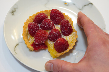 A hand grabbing a delicious lemon and raspberry tart. sweet treat dessert. 
