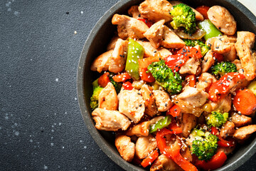 Chicken stir fry with vegetables and sesame at black background. Close up.