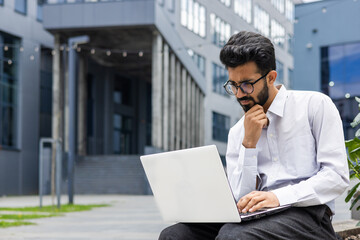 An attentive male entrepreneur works on his laptop outdoors, deeply engrossed in a task, with a...