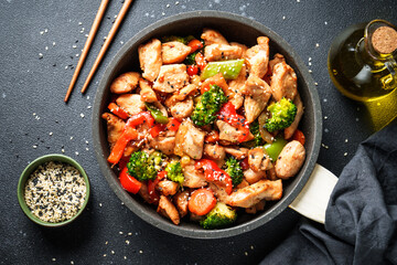 Chicken stir fry with vegetables and sesame at black background. Traditional asian cuisine.