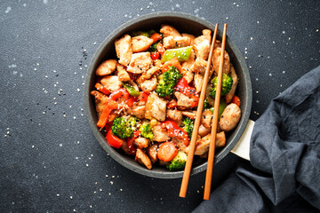 Chicken stir fry with vegetables and sesame at black background. Traditional asian cuisine.