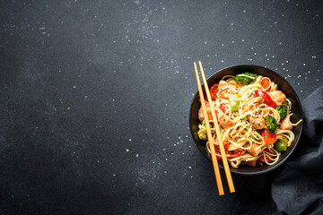 Asian noodles with chicken and vegetables at black background. Top view with space for design.