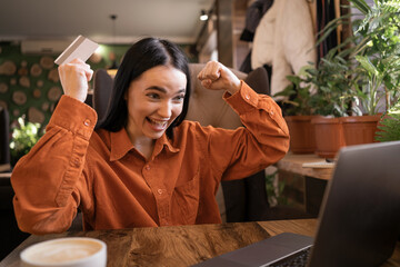 Euphoric shopper buying online with laptop and credit card sitting in cafe with cup of coffee.