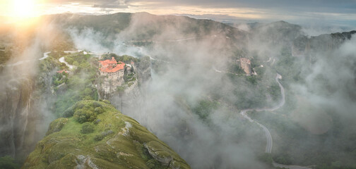 Panoramic, aerial view of Meteora landscape with Holy Varlaam Monastery, rising from a morning fog,...
