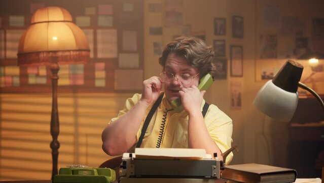 important man in retro style talks on an old telephone and puts on glasses. Vintage office in which a man speaks on the phone with an interlocutor. Editorial office or production plant.