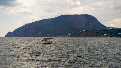 The boat is anchored in the open sea against the backdrop of a mountain.