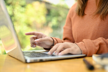 Female freelancer in brown sweater typing on laptop, searching information or working online