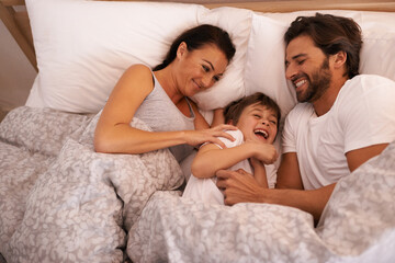 Obraz na płótnie Canvas Parents, boy and tickling with laughing in bed for care, bonding or love with joke in family house. Father, mother and child with funny game, excited or happy for comic smile together in home bedroom