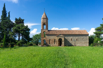 Saint Giorgi church on a green grass lawn against the background of a blue sky with clouds.
