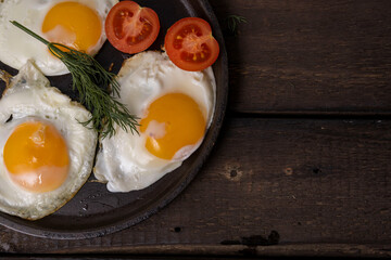 Fried eggs in a pan with vegetables and herbs on a black background.