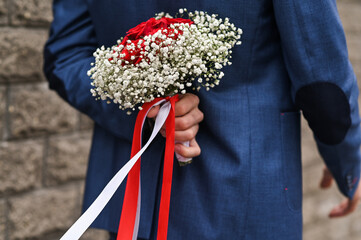 The groom holds flowers behind his back for the bride