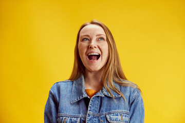 Portrait of young emotional woman in denim jacket posing against yellow studio background. Concept...
