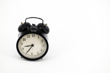 A black alarm clock with two bells on top, chrome handle, and legs, set against a white background. Timeless design meets functionality in this sleek, monochromatic timepiece..