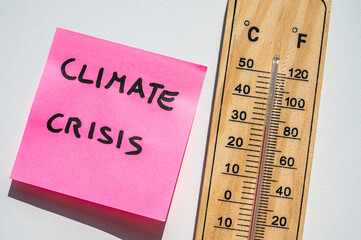 Thermometer on a light surface, and next to a note with the text Climate Crisis. Global warming.